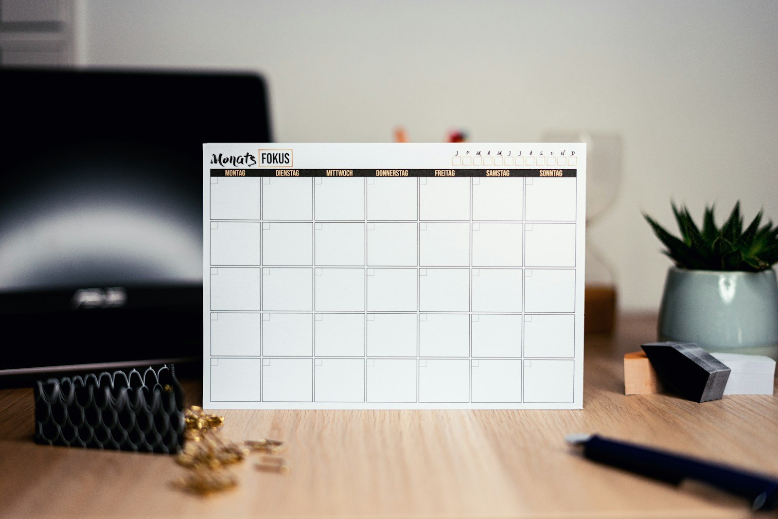 Fotografia ilustrativa de um calendário de papel em uma mesa de trabalho, com computador ao fundo.